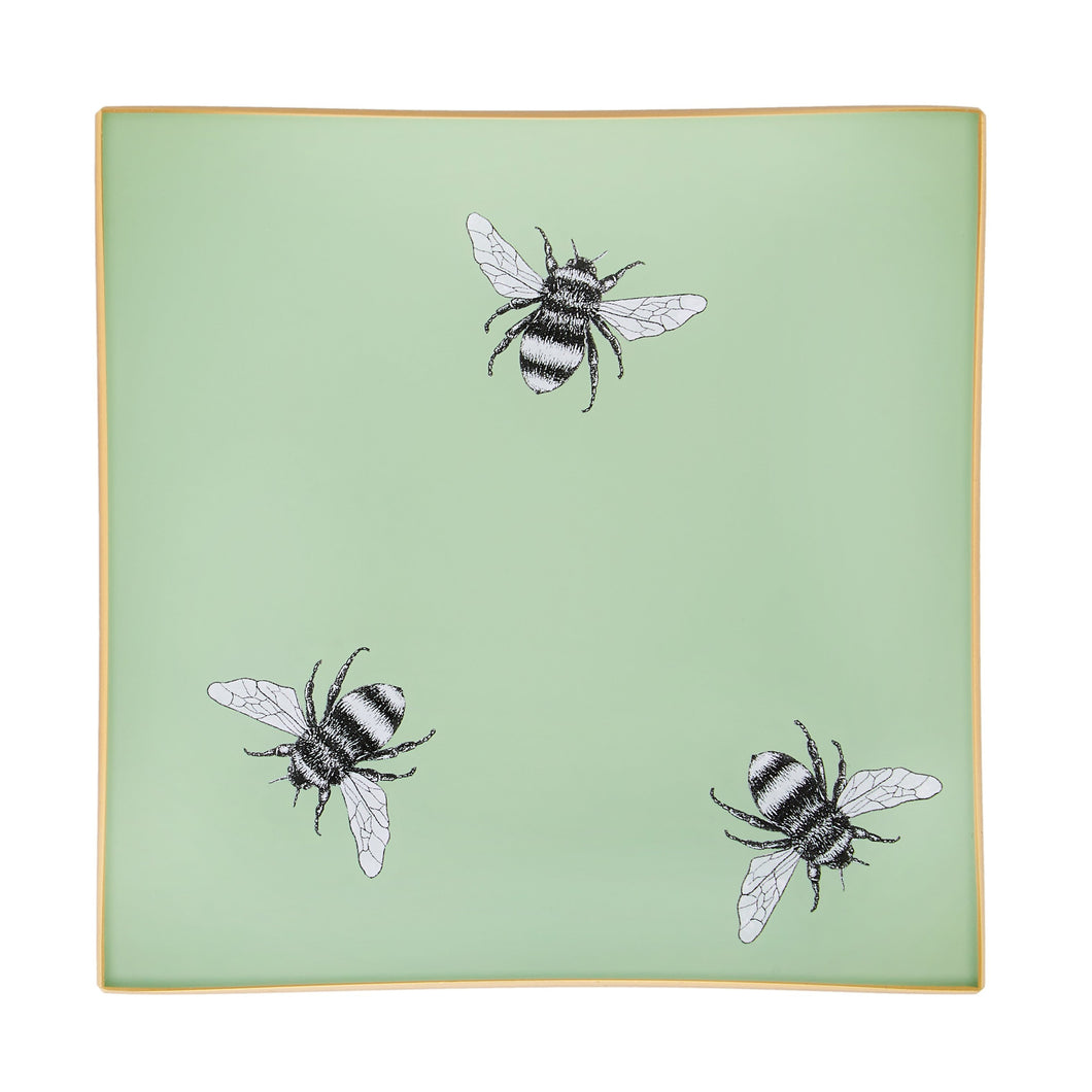 An artisanal, decorative glass valet tray with three bee illustrations on a pale sage green background finished with an 18kt gold leaf edging