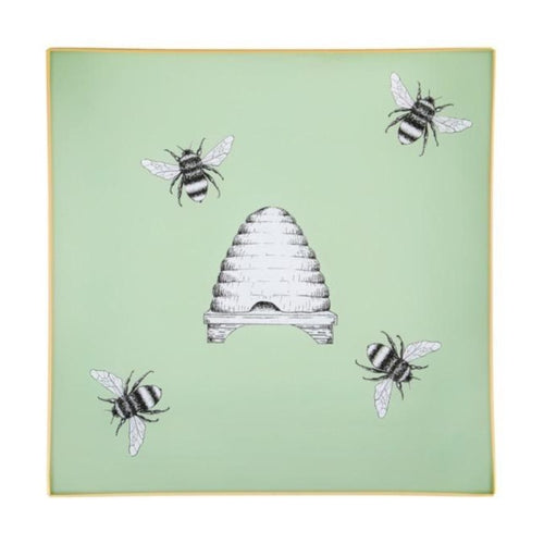 An artisanal, decorative glass valet tray with illustrations of four bees surrounding a bee hive on a pale sage green background finished with an 18kt gold leaf edging