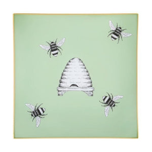 An artisanal, decorative glass valet tray with illustrations of four bees surrounding a bee hive on a pale sage green background finished with an 18kt gold leaf edging